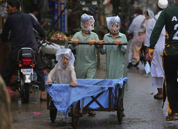 Crianças paquistanesas usam sacos plásticos para cobrirem suas cabeças durante a chuva em Peshawar, Paquistão - Sputnik Brasil