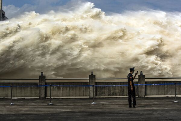 Guarda chinês é visto olhando para seu smartphone enquanto a usina hidrelétrica das Três Gargantas, uma das maiores do mundo, libera água em Yichang, na província chinesa de Hubei - Sputnik Brasil
