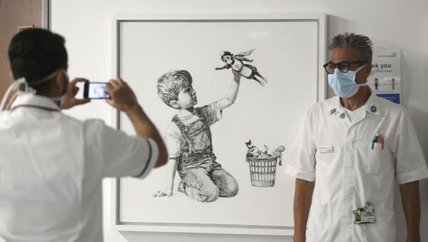 Um membro da equipe tira uma foto em frente à nova obra de arte pintada por Banksy durante o isolamento social, intitulada 'Game Changer', que foi exibida para funcionários e pacientes no Nível C do Hospital Geral de Southampton, em Southampton, Inglaterra, durante maio de 2020. - Sputnik Brasil