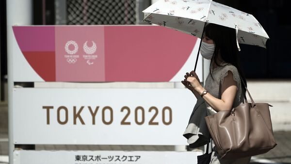 Mulher usando máscara caminha em frente a logotipo dos Jogos Olímpicos de Tóquio 2020, que foram adiados para 2021 devido à pandemia do novo coronavírus - Sputnik Brasil