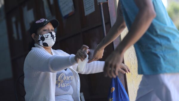 Enfermeira joga spray de álcool para higienizar clientes contra coronavírus em mercado em Caracas, na Venezuela - Sputnik Brasil