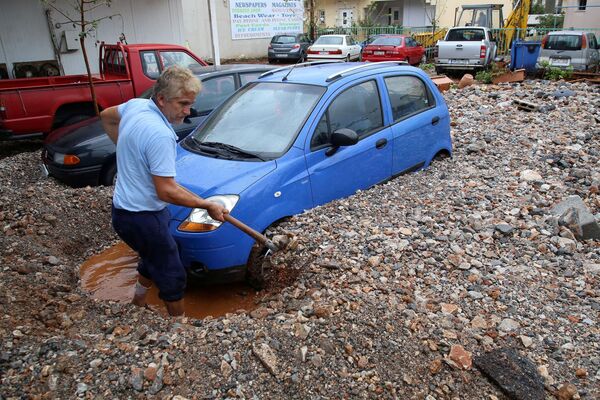 Homem remove pedras ao redor de seu carro após fortes chuvas atingirem Creta, na Grécia - Sputnik Brasil
