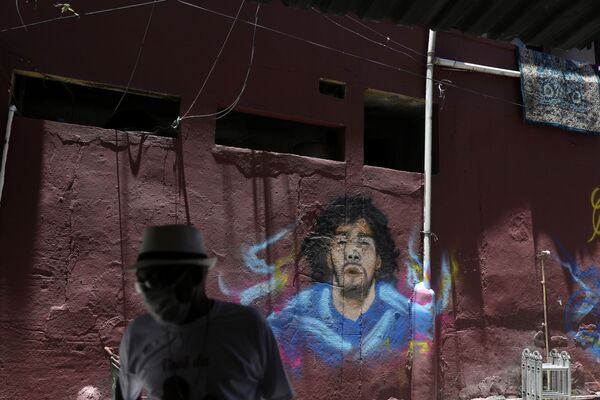 Homem com máscara para se proteger da COVID-19 diante de muro com grafite do jogador argentino Diego Maradona, no Rio de Janeiro - Sputnik Brasil