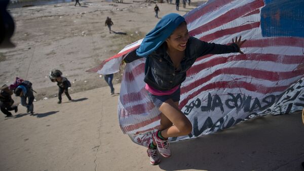 Imigrante ajuda a levar a bandeira norte-americana à fronteira entre o México e os EUA, depois de ter ultrapassado a polícia mexicana na fronteira. A construção de um muro fronteiriço entre os EUA e o México mais fortificado foi uma das promessas da campanha eleitoral de Trump de 2016 - Sputnik Brasil