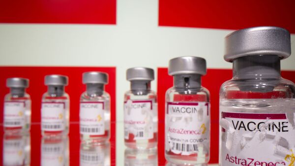 Vials labelled with broken sticker AstraZeneca COVID-19 Coronavirus Vaccine are seen in front of a displayed Denmark flag in this illustration taken March 15, 2021. - Sputnik Brasil