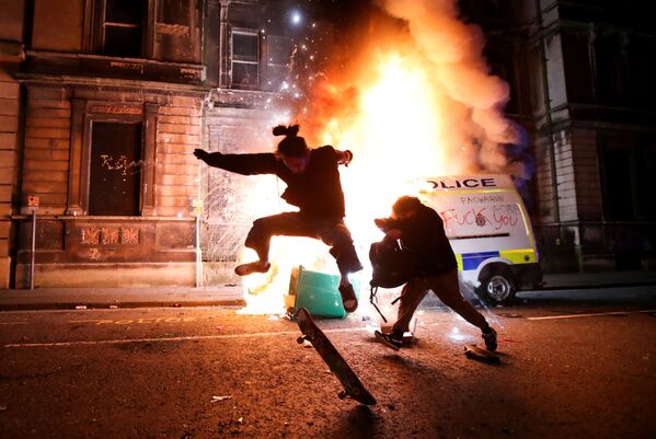 Manifestante anda de skate na frente de um carro da polícia em chamas durante protesto no Reino Unido
 - Sputnik Brasil