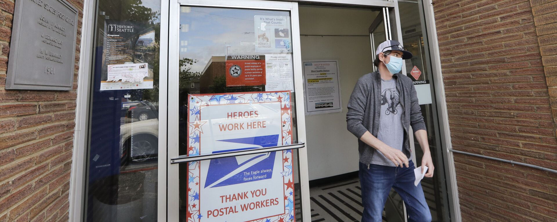 um cliente sai de uma agência dos Correios dos EUA e sob um banner anunciando uma vaga de emprego, em Seattle, EUA - Sputnik Brasil, 1920, 06.09.2025