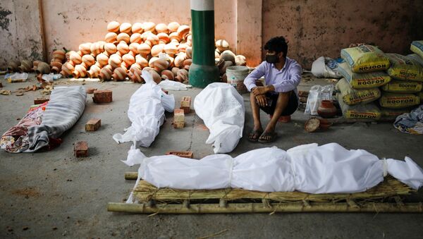 Em Nova Deli, na Índia, um homem aparece sentado próximo de corpos de pessoas infectadas com a COVID-19 enquanto aguarda a cremação dos mortos, em 26 de abril de 2021 - Sputnik Brasil