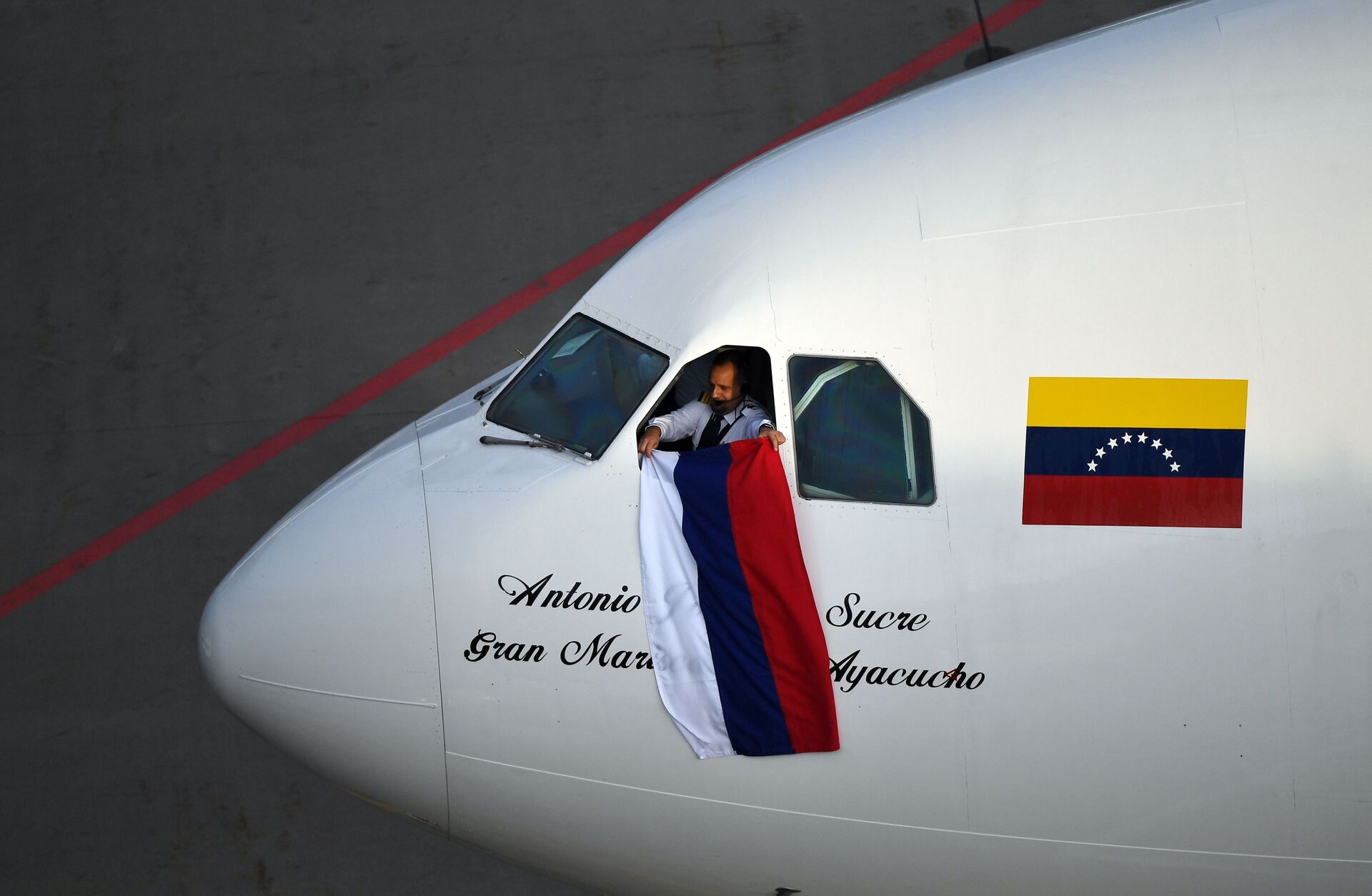 Em Moscou, um piloto da companhia aérea venezuelana Conviasa mostra uma bandeira da Rússia após a chegada ao aeroporto de Vnukovo no primeiro voo da rota direta entre a capital russa e Caracas, em 15 de maio de 2021 - Sputnik Brasil, 1920, 25.01.2022