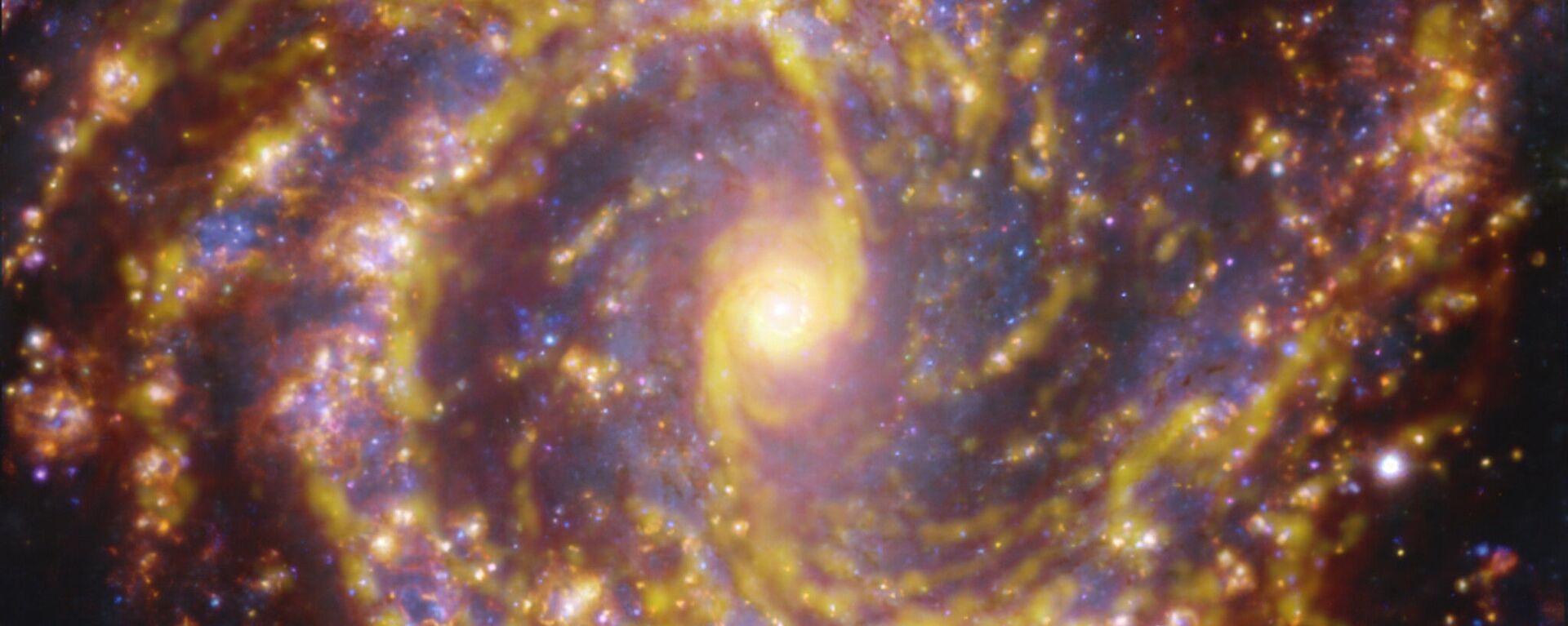 Galáxia NGC 4303 próxima à Via Láctea. NGC 4303 é uma galáxia espiral, com uma barra de estrelas e gás em seu centro, localizada a aproximadamente 55 milhões de anos-luz da Terra, na constelação Virgo. A imagem é uma combinação de observações realizadas em diferentes comprimentos de onda de luz para mapear populações estelares e gás. As observações do telescópio ALMA são representadas em tons marrom-alaranjados e destacam as nuvens de gás molecular frio que fornecem a matéria-prima a partir da qual as estrelas se formam. Os dados do espetrógrafo MUSE aparecem principalmente em dourado e azul. Os brilhantes dourados mapeiam nuvens quentes, principalmente de hidrogênio ionizado, oxigênio e gás sulfúrico, marcando a presença de estrelas recém-nascidas, enquanto as regiões azuis revelam a distribuição de estrelas ligeiramente mais velhas - Sputnik Brasil, 1920, 22.07.2025