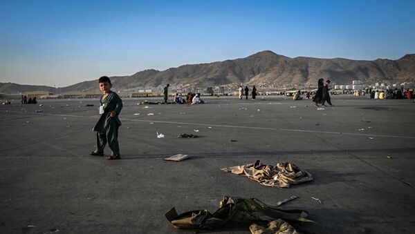 Criança afegã caminha perto de uniformes militares no aeroporto de Cabul, em 16 de agosto de 2021 - Sputnik Brasil
