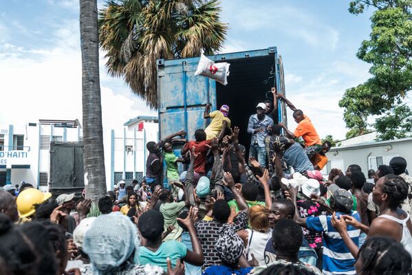 Homem joga saco de arroz para multidão durante distribuição de alimentos e água entre vítimas do terremoto em Les Cayes, Haiti
 - Sputnik Brasil