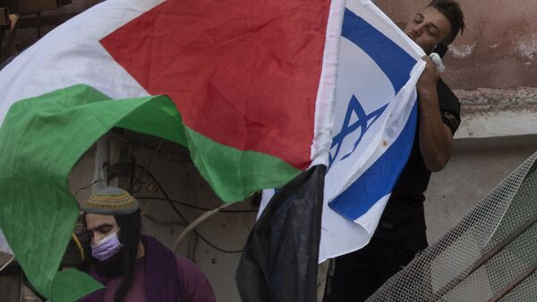 Um homem beija a bandeira israelense enquanto manifestantes agitam a bandeira palestina no portão da frente de uma casa palestina ocupada por judeus israelenses, 26 de maio de 2021 - Sputnik Brasil