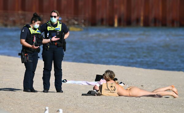 Policiais falam com mulher tomando banhos de sol na praia de St. Kilda, em Melbourne durante o regime de quarentena na Austrália. - Sputnik Brasil