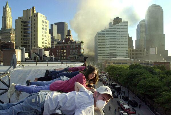 Pessoas no telhado de um prédio olham para a rua cheia de equipes de resgate, em meio à fumaça no local do ataque terrorista, Nova York, 12 de setembro de 2001. - Sputnik Brasil