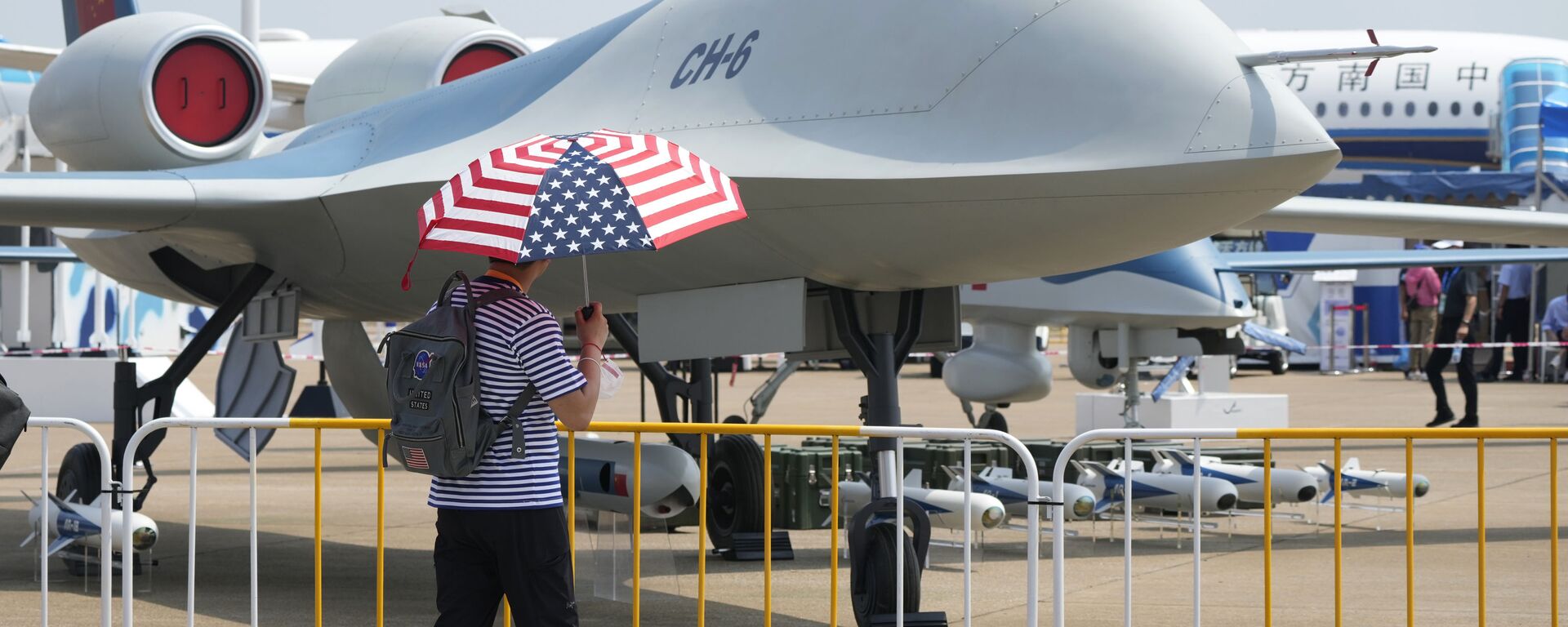 Homem com guarda-chuva com o desenho da bandeira dos EUA passa por um drone CH-6, em 28 de setembro de 2021 - Sputnik Brasil, 1920, 08.08.2024