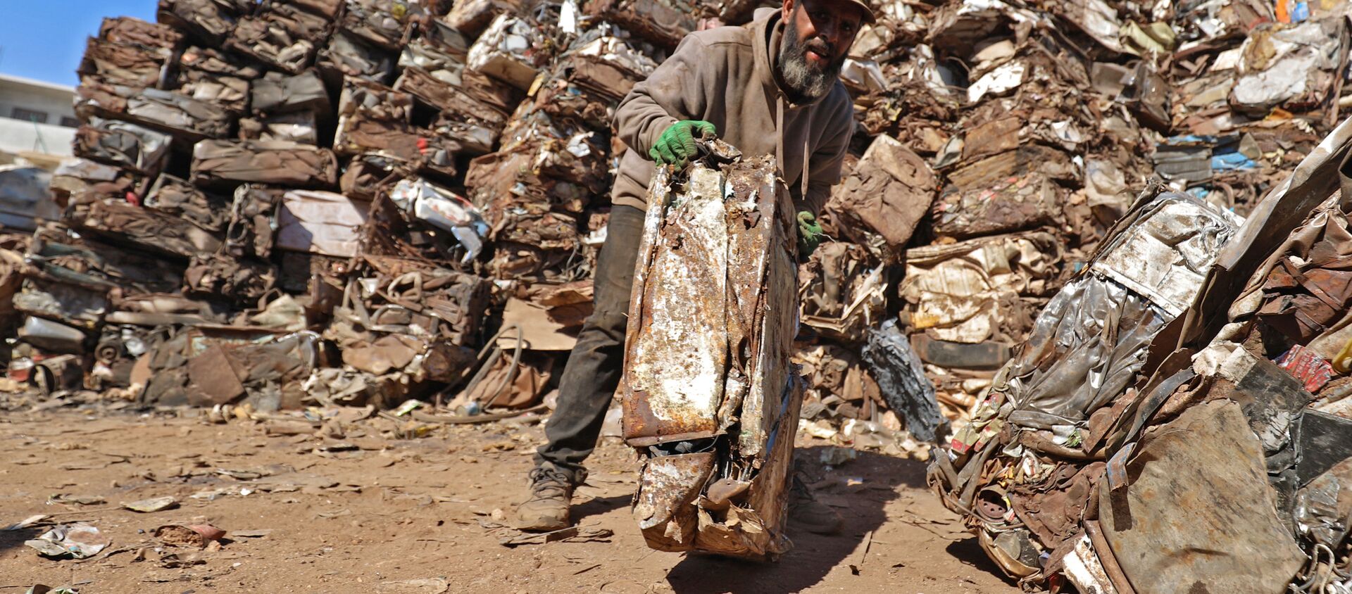 Homem caminha com sucata compactada na cidade de Batabu, zona rural das províncias de Idlib e Aleppo, Síria, 5 de outubro de 2021 - Sputnik Brasil, 1920, 07.10.2021