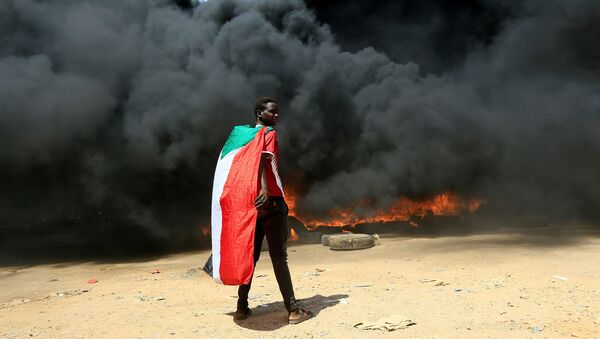 Manifestante com bandeira do Sudão na frente de uma pilha de pneus em chamas durante protestos em Cartum, 21 de outubro de 2021 - Sputnik Brasil