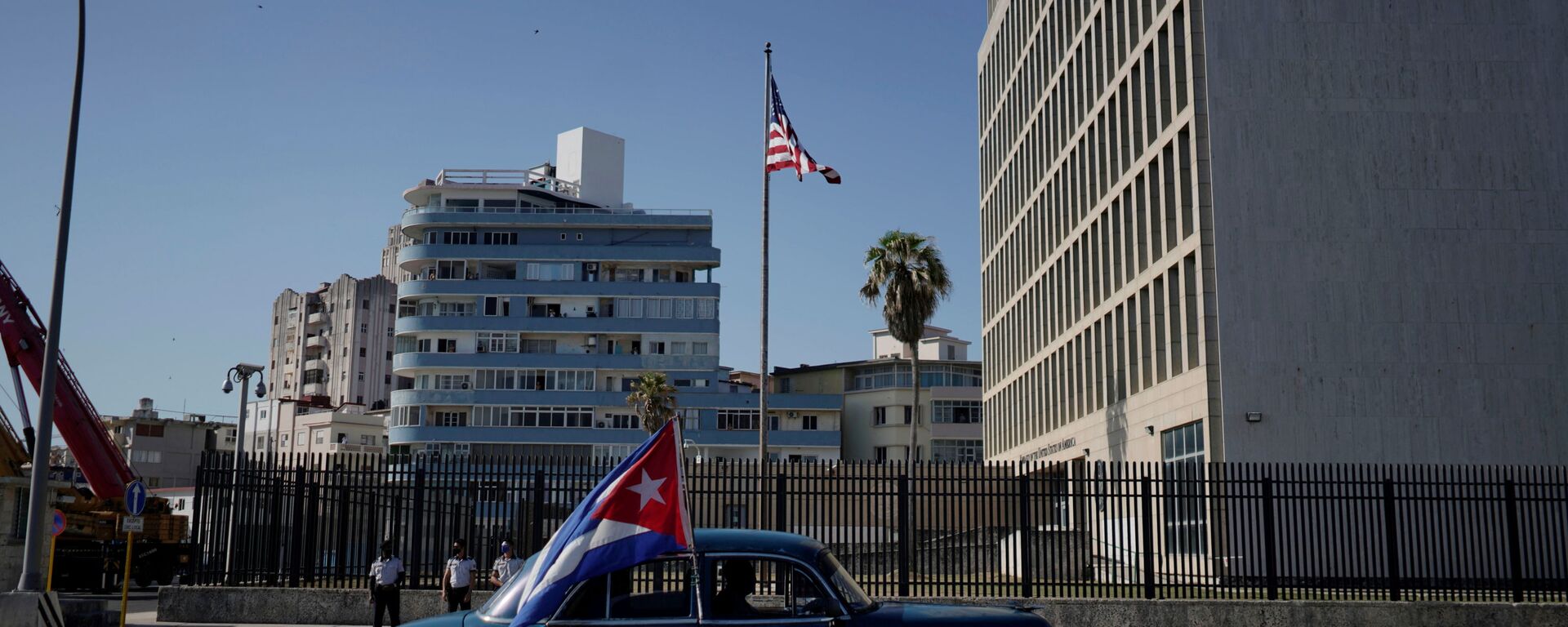 Carro antigo passa pela embaixada dos EUA carregando uma bandeira cubana durante carreata de protesto contra o embargo contra Cuba pelos EUA, Havana, 28 de março de 2021 - Sputnik Brasil, 1920, 13.02.2026