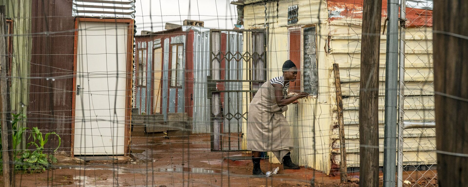 Moradora do assentamento de Vlakfontein, nos arredores de Joanesburgo, África do Sul, fecha sua janela durante uma tempestade 
 - Sputnik Brasil, 1920, 09.08.2024