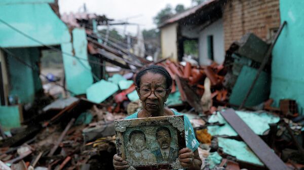 Em Itambé, no estado brasileiro da Bahia, Vitória Rocha, de 81 anos, segura uma foto de seus pais em frente aos escombros de sua casa destruída por enchentes, em 28 de dezembro de 2021 - Sputnik Brasil