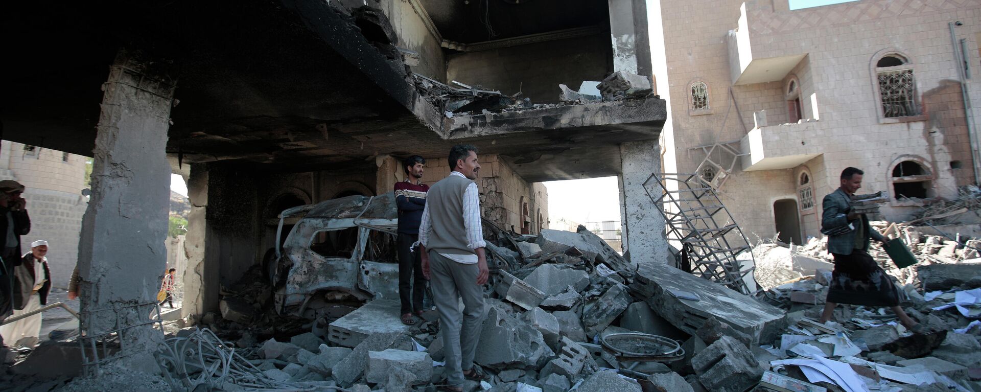 Pessoas inspecionam os destroços de edifícios que foram danificados por ataques aéreos da coalizão liderada pela Arábia Saudita, em Sanaa, Iêmen, terça-feira, 18 de janeiro de 2022 - Sputnik Brasil, 1920, 21.01.2022