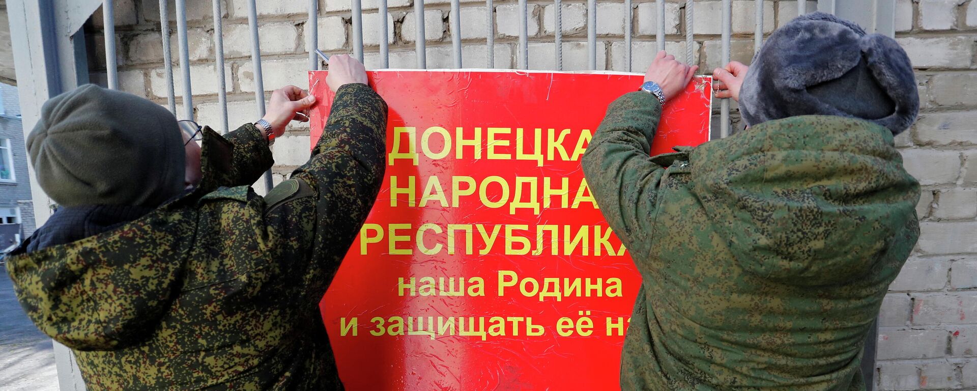 Militares da autoproclamada República Popular de Donetsk pendurando faixa nas portas de uma escola que diz: A República Popular de Donetsk é nossa pátria e nós devemos defendê-la!, Donetsk, 19 de fevereiro de 2022 - Sputnik Brasil, 1920, 20.02.2022