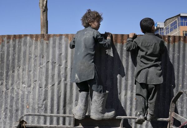 Garotos espreitam pessoas recebendo provisões alimentares sobre barreira de metal em Cabul, Afeganistão, 16 de fevereiro de 2022 - Sputnik Brasil