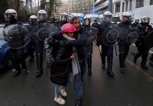 Homem segura mulher enquanto caminham à frente de policiais em equipamento antimotim durante protestos contra restrições da COVID-19 junto de instituições da União Europeia em Bruxelas, Bélgica, 14 de fevereiro de 2022 - Sputnik Brasil