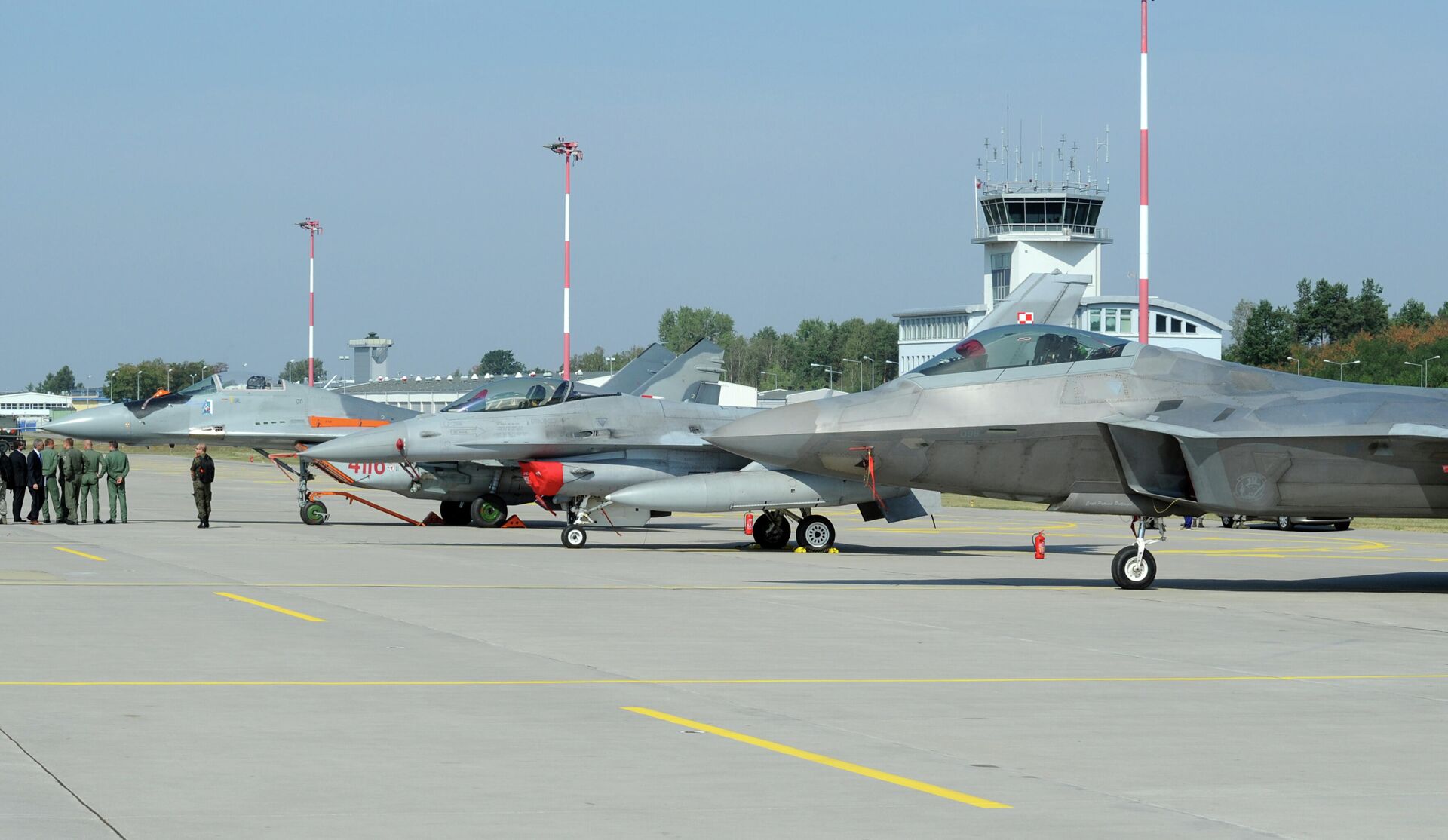 Autoridades passam por caças estacionados no pátio, um Mig-29 da Força Aérea Polonesa, à esquerda, um F-16 da Força Aérea Polonesa, ao centro e um F-22 Raptor dos EUA em uma base militar em Lask, Polônia, segunda-feira, 31 de agosto de 2015 - Sputnik Brasil, 1920, 04.06.2022