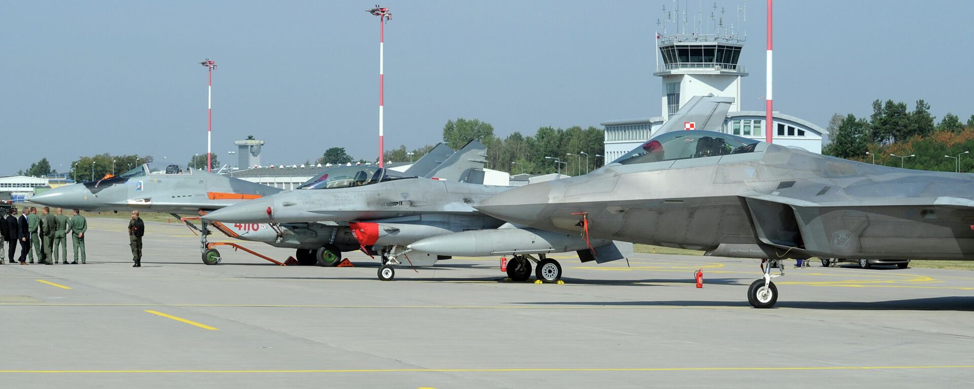Autoridades passam por caças estacionados no pátio, um Mig-29 da Força Aérea Polonesa, à esquerda, um F-16 da Força Aérea Polonesa, ao centro e um F-22 Raptor dos EUA em uma base militar em Lask, Polônia, segunda-feira, 31 de agosto de 2015 - Sputnik Brasil, 1920, 23.04.2023