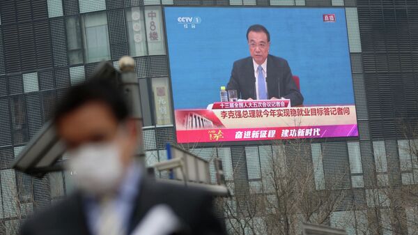 Em Pequim, um homem de máscara caminha com um telão ao fundo que transmite discurso do premiê chinês, Li Keqiang, após o encerramento da sessão Congresso Nacional do Povo, em 11 de março de 2022 - Sputnik Brasil