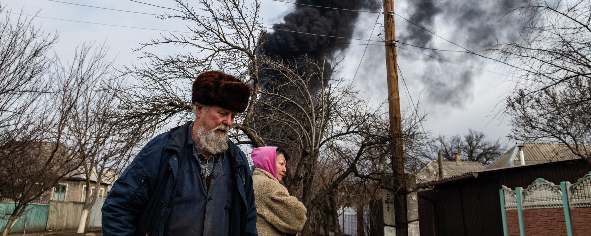 Em Lugansk, na República Popular de Lugansk (RPL), duas pessoas caminham, com uma coluna de fumaça ao fundo, em 7 de março de 2022. - Sputnik Brasil, 1920, 15.03.2022