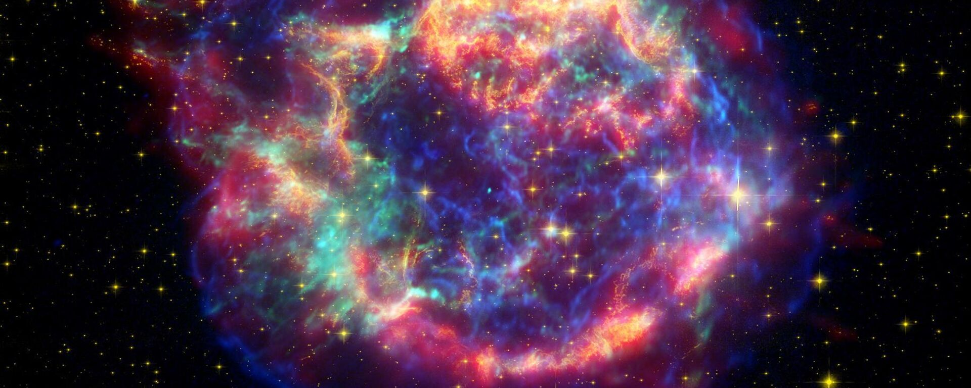 Imagem de Cassiopeia A composta por dados infravermelhos do Telescópio Espacial Spitzer (tons de vermelho), do Telescópio Espacial Hubble (tons de dourado) e do Observatório de Raios-X Chandra (tons de azul e verde). O pequeno e brilhante ponto azul-bebê fora do centro é o remanescente do núcleo da estrela - Sputnik Brasil, 1920, 29.03.2022
