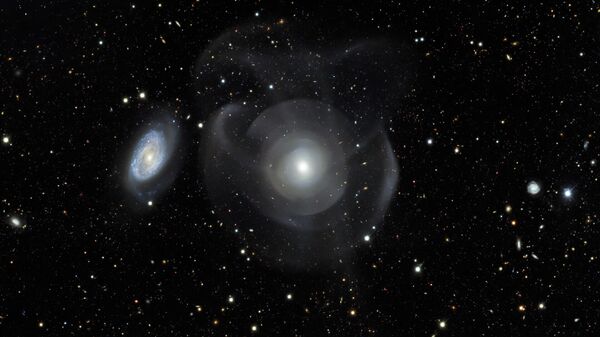 Galáxias elípticas como a NGC 474 são geralmente caracterizadas por sua aparência relativamente lisa quando comparadas com galáxias espirais (à esquerda), com estruturas floculentas entrelaçadas com faixas de poeira e braços espirais - Sputnik Brasil