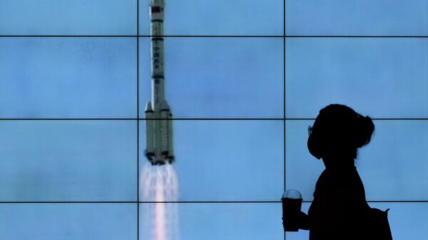 Uma pessoa de máscara caminha em frente a uma tela mostrando um lançamento do foguete Longa Marcha-2F Y12 em uma transmissão da CCTV, em Pequim, China, 17 de junho de 2021 - Sputnik Brasil