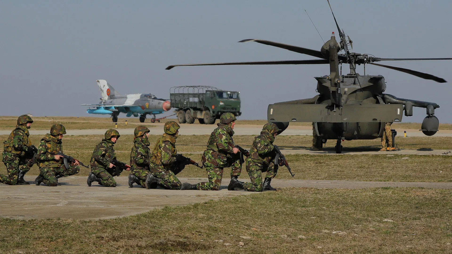 Com um jato de combate MIG 21 e um helicóptero Blackhawk ao fundo, soldados dos EUA participam de exercício militar conjunto com as Forças Armadas romenas na base aérea de Mihail Kogalniceanu, Romênia, 8 de março de 2017 Com um jato de combate MIG 21 e um helicóptero Blackhawk ao fundo, soldados dos EUA participam de exercício militar conjunto com as Forças Armadas romenas na base aérea de Mihail Kogalniceanu, Romênia, 8 de março de 2017 - Sputnik Brasil, 1920, 23.07.2026