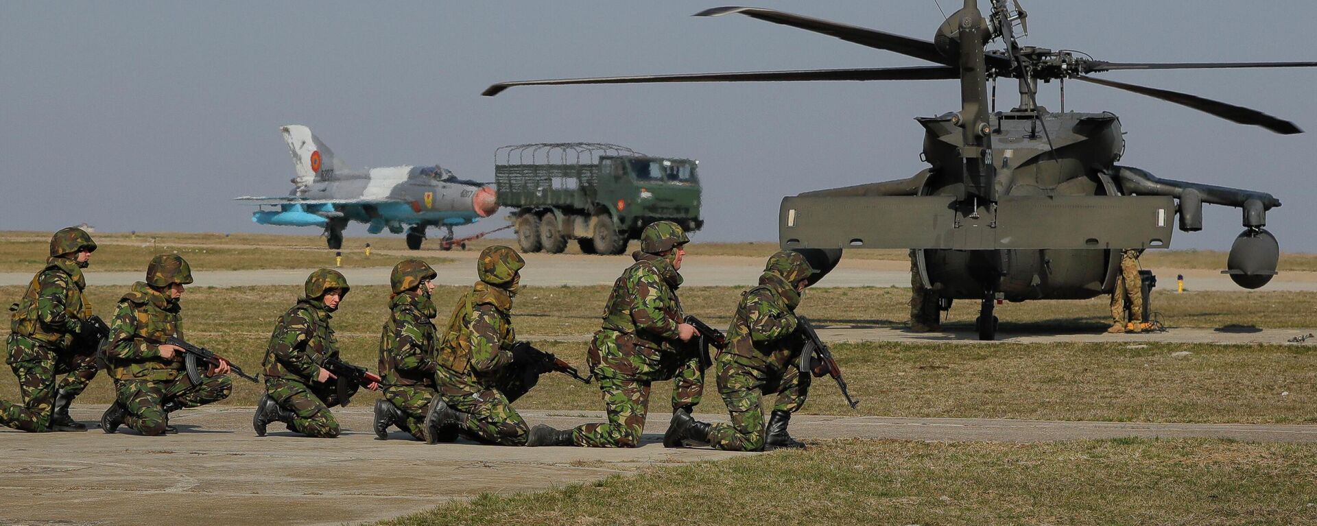 Com um jato de combate MIG 21 e um helicóptero Blackhawk ao fundo, soldados dos EUA participam de exercício militar conjunto com as Forças Armadas romenas na base aérea de Mihail Kogalniceanu, Romênia, 8 de março de 2017 - Sputnik Brasil, 1920, 14.12.2022