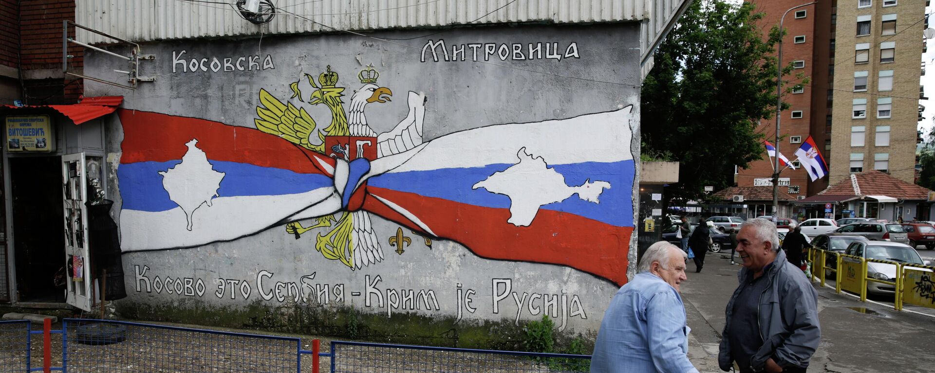 Pessoas descansam ao lado de grafite com os escritos Kosovo é Sérvia, Crimeia é Rússia, em Kosovska Mitrovica, Sérvia, em 28 de maio de 2019 - Sputnik Brasil, 1920, 10.09.2022