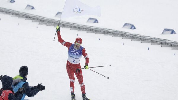 Sergei Ustiugov da Rússia voa até a linha de chegada segurando a bandeira do Comitê Olímpico Russo no evento de revezamento 4x10 km masculino durante os Jogos Olímpicos de Inverno de Pequim 2022, Centro Nacional de Esqui Cross-Country Zhangjiakou, 13 de fevereiro de 2022 - Sputnik Brasil