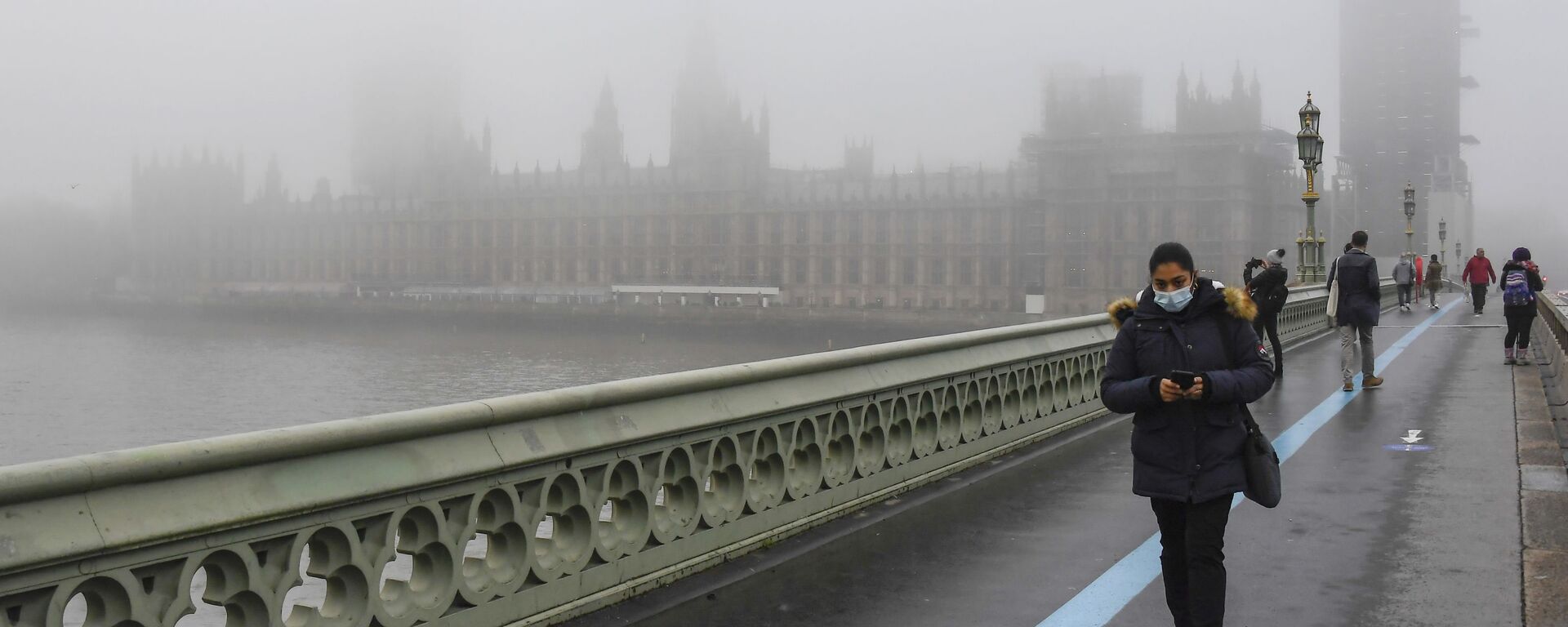 Pessoas usando máscaras faciais caminham pela Westminster Bridge com as Casas do Parlamento envoltas em neblina, em Londres, Reino Unido, 8 de dezembro de 2020 - Sputnik Brasil, 1920, 21.11.2022