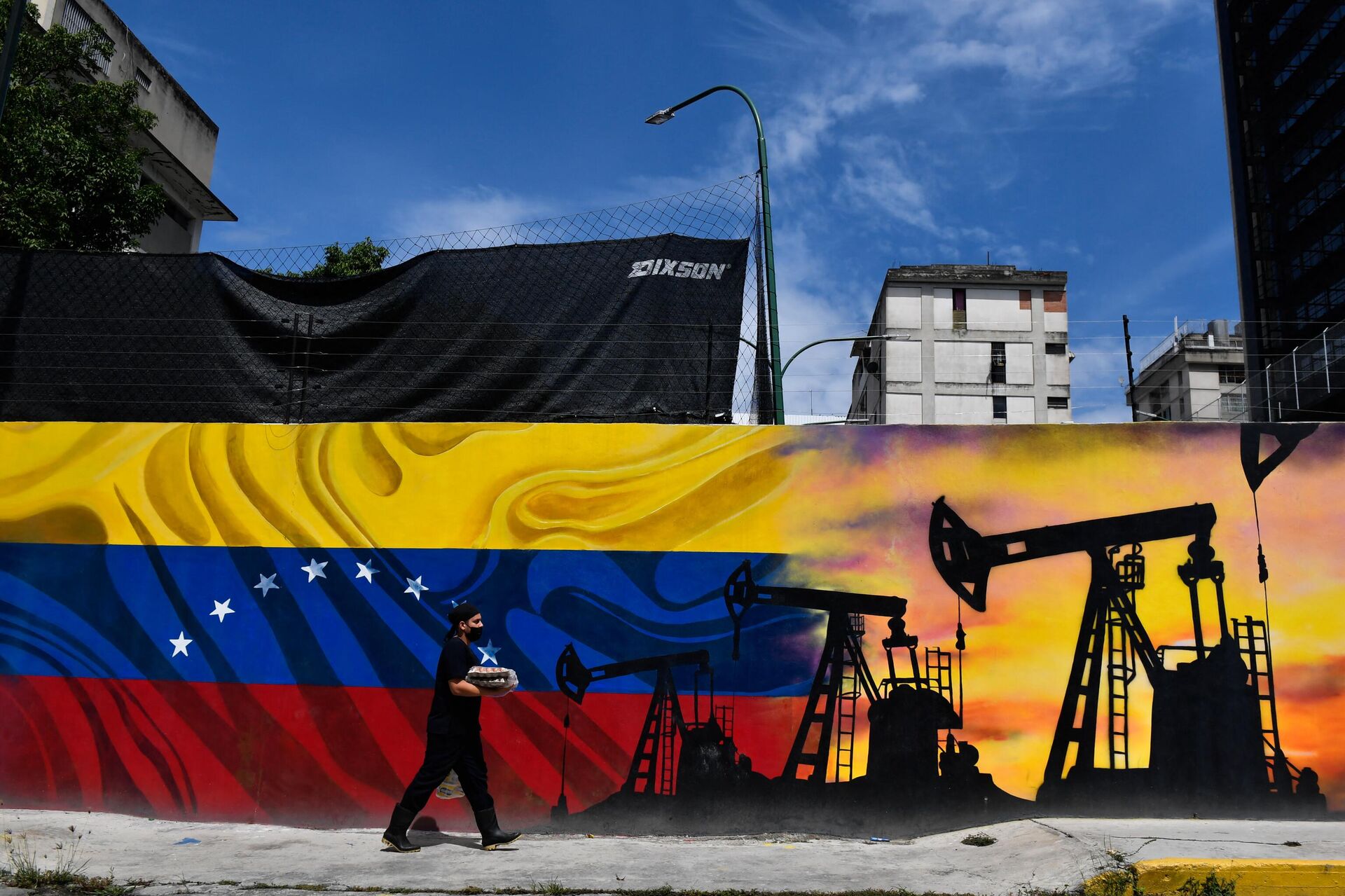 Um homem usando uma máscara facial passa por um mural representando uma bomba de petróleo e a bandeira venezuelana, em uma rua de Caracas, em 26 de maio de 2022 - Sputnik Brasil, 1920, 09.08.2024