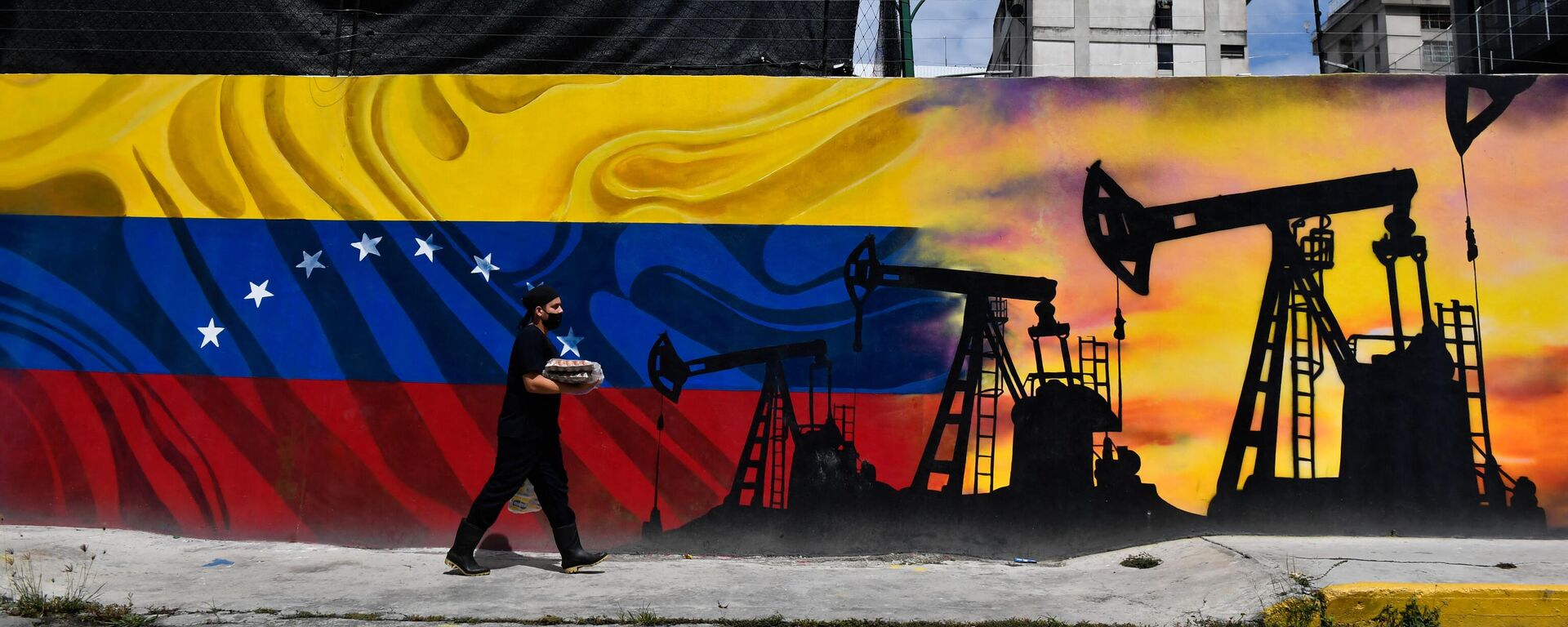Um homem usando uma máscara facial passa por um mural representando uma bomba de petróleo e a bandeira venezuelana, em uma rua de Caracas, em 26 de maio de 2022 - Sputnik Brasil, 1920, 07.07.2023