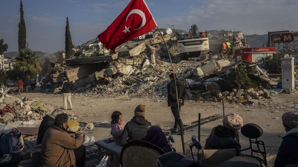 Família sentada junto de prédio colapsado após terremoto, em Antália, Turquia, 11 de fevereiro de 2023 - Sputnik Brasil