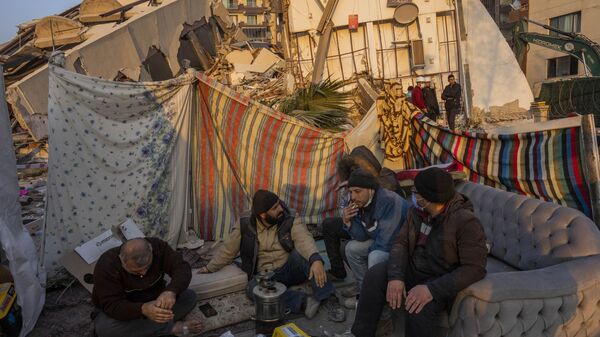 Homens se sentam em frente aos escombros de uma área destruída durante o terremoto em Antakya, sudeste da Turquia, 12 de fevereiro de 2023 - Sputnik Brasil