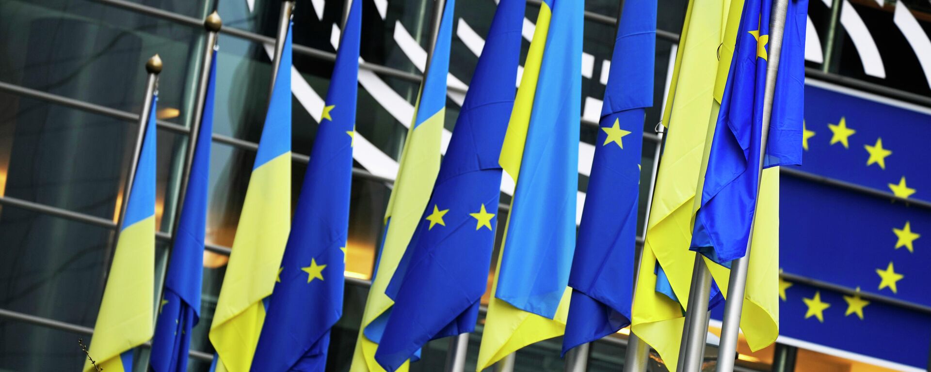 Bandeiras da Ucrânia e da União Europeia (UE) penduradas juntas no exterior do edifício antes de uma sessão plenária extraordinária sobre a Ucrânia no Parlamento Europeu em Bruxelas, 1º de março de 2022 - Sputnik Brasil, 1920, 26.03.2023