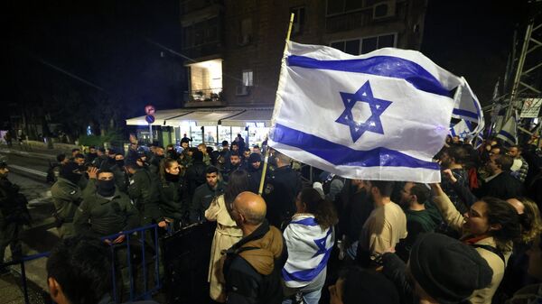 Manifestantes entoam slogans e agitam bandeiras durante uma manifestação contra a reforma judicial do governo israelense no exterior da residência do primeiro-ministro Benjamin Netanyahu em Jerusalém, em 27 de março de 2023 - Sputnik Brasil