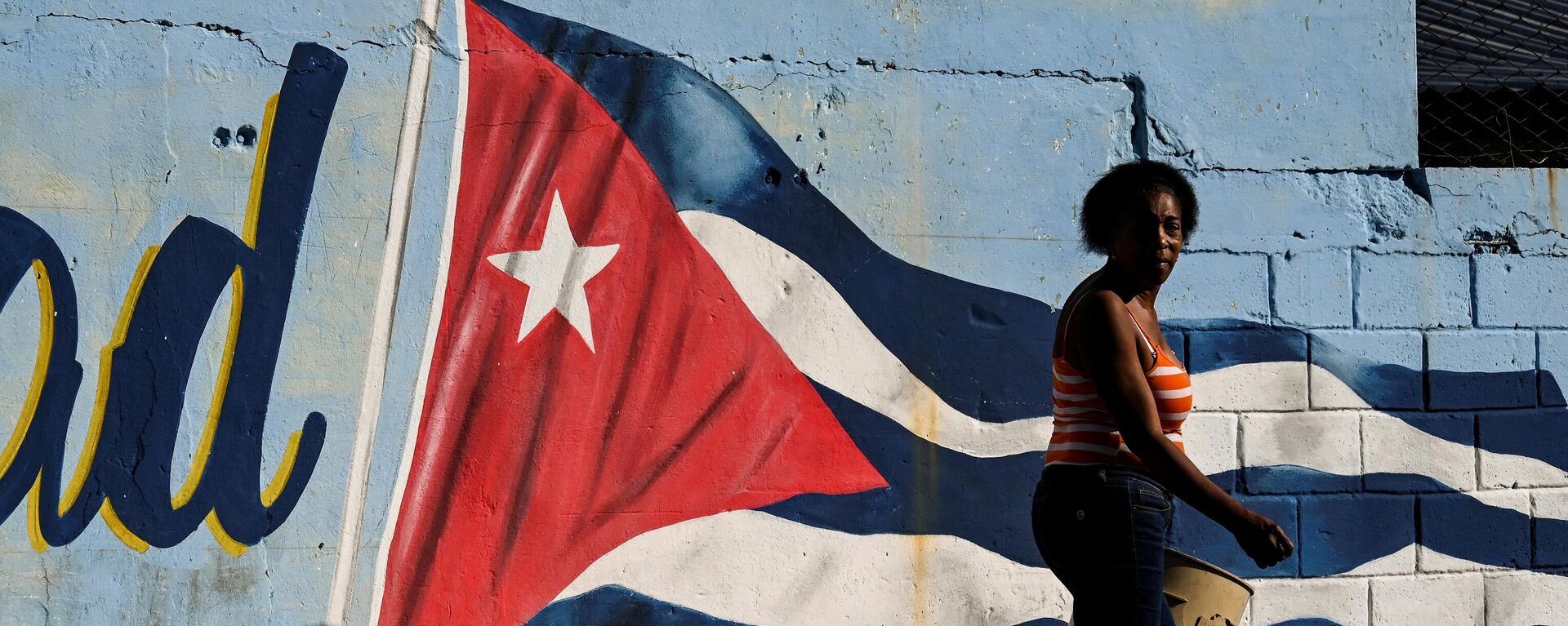 Uma mulher passa por uma parede pintada com a bandeira cubana com a legenda continuidade em Havana, 7 de fevereiro de 2023 - Sputnik Brasil, 1920, 19.04.2023
