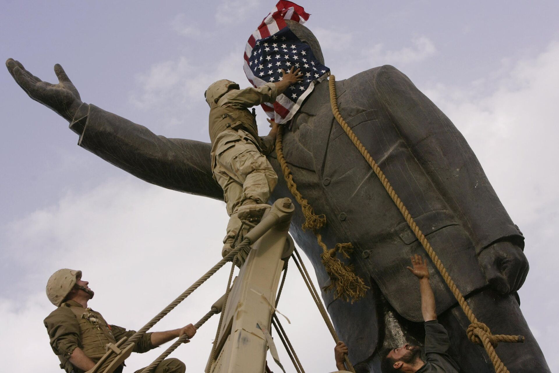Soldados norte-americanos cobrem o rosto de uma estátua de Saddam Hussein com uma bandeira dos EUA antes de derrubar a estátua no centro de Bagdá no auge da Guerra no Iraque, Iraque, 9 de abril de 2003 - Sputnik Brasil, 1920, 23.06.2023