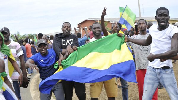 Moradores gesticulam e seguram uma bandeira nacional do Gabão enquanto comemoram em Libreville, em 30 de agosto de 2023 - Sputnik Brasil